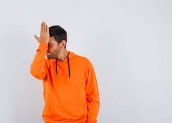 Homem cobrindo o rosto com a mão demonstrando frustração, simbolizando erros de julgamento ligados à armadilha da inteligência e vieses cognitivos.