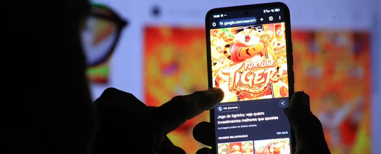 Pessoa utilizando smartphone exibindo jogo de aposta online relacionado ao “tigrinho” em ambiente digital.