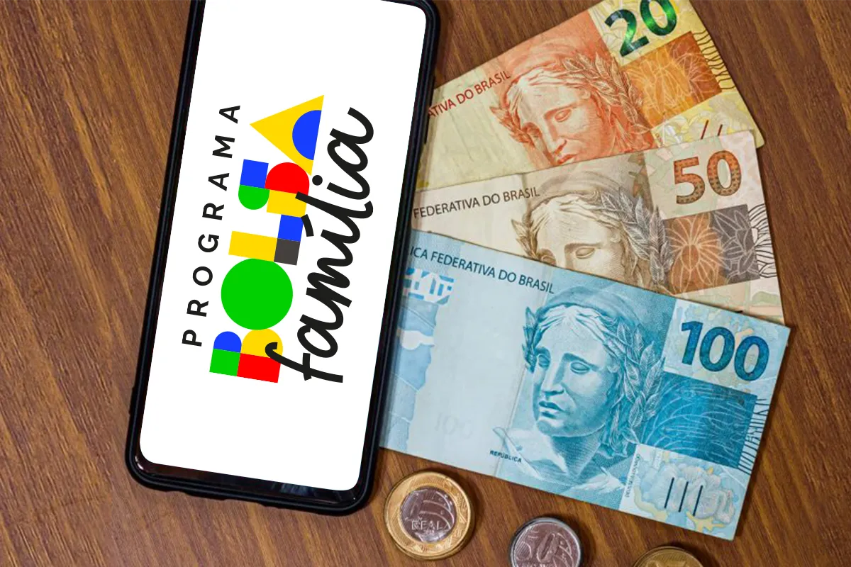 Celular com logo do Programa Bolsa Família sobre notas de R$ 100, R$ 50, R$ 20 e moedas.