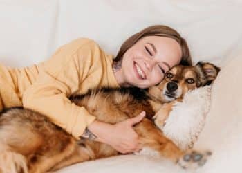 Jovem abraça cachorro sorrindo em momento de carinho no sofá.