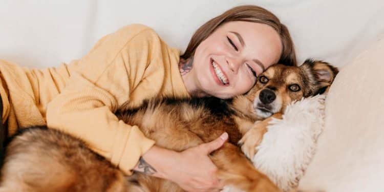 Jovem abraça cachorro sorrindo em momento de carinho no sofá.