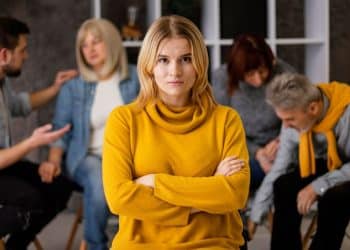 Mulher de blusa amarela com braços cruzados afastada de outras pessoas.