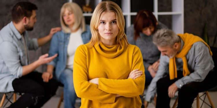 Mulher de blusa amarela com braços cruzados afastada de outras pessoas.