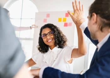 Profissional jovem comemorando resultado com colega em ambiente corporativo moderno.