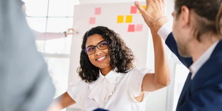 Profissional jovem comemorando resultado com colega em ambiente corporativo moderno.