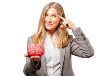 Mulher madura apontando para a cabeça e segurando objeto que simula o cérebro humano.