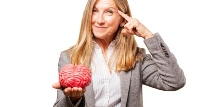 Mulher madura apontando para a cabeça e segurando objeto que simula o cérebro humano.