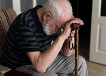 Homem idoso demonstrando preocupação, com a cabeça abaixada, possivelmente reflexo de uma situação angustiante relacionada a fraudes contra beneficiários do INSS.