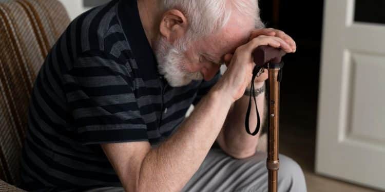 Homem idoso demonstrando preocupação, com a cabeça abaixada, possivelmente reflexo de uma situação angustiante relacionada a fraudes contra beneficiários do INSS.
