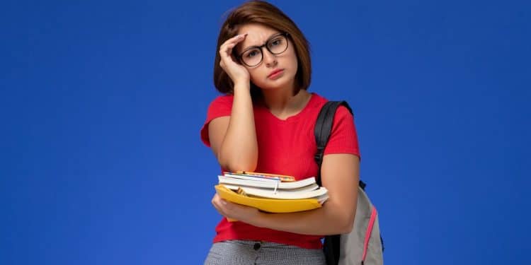 Estudante cansada segura livros e cadernos com expressão de estresse
