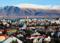 Vista panorâmica de cidade na Islândia com casas coloridas e montanhas nevadas ao fundo, representando qualidade de vida e bem-estar.