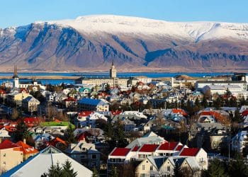Vista panorâmica de cidade na Islândia com casas coloridas e montanhas nevadas ao fundo, representando qualidade de vida e bem-estar.