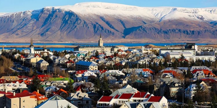 Vista panorâmica de cidade na Islândia com casas coloridas e montanhas nevadas ao fundo, representando qualidade de vida e bem-estar.