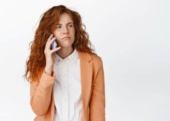 Mulher ruiva ao telefone com expressão de desconfiança.