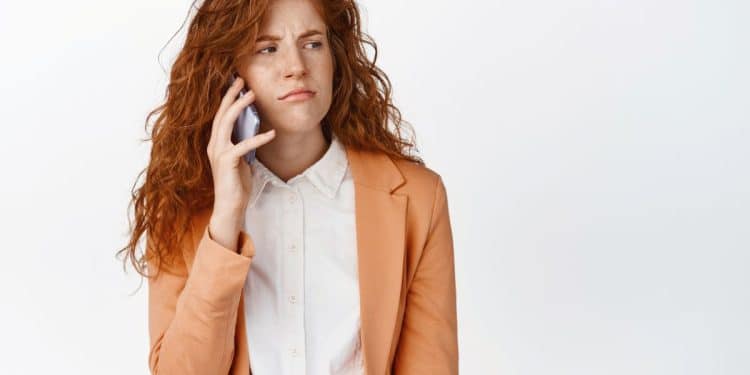Mulher ruiva ao telefone com expressão de desconfiança.
