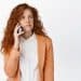 Mulher ruiva ao telefone com expressão de desconfiança.