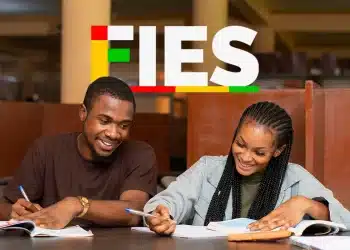 Dois jovens estudantes negros escrevem e sorriem em biblioteca com logo do FIES ao fundo.