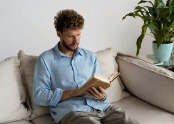 Homem lendo livro no sofá da sala.