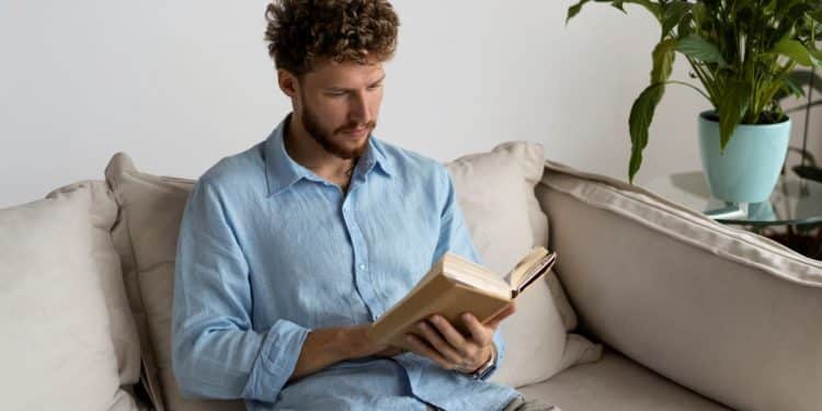 Homem lendo livro no sofá da sala.