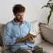 Homem lendo livro no sofá da sala.