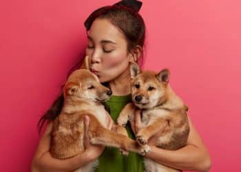 Mulher segurando dois filhotes de cachorro enquanto demonstra carinho, ilustrando diferenças entre masculino e feminino nos nomes de animais.