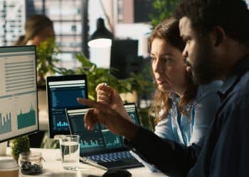 Líder de equipe orientando colaborador sobre ajustes em documentos e gráficos, refletindo o papel de liderar decisões estratégicas baseadas em dados.