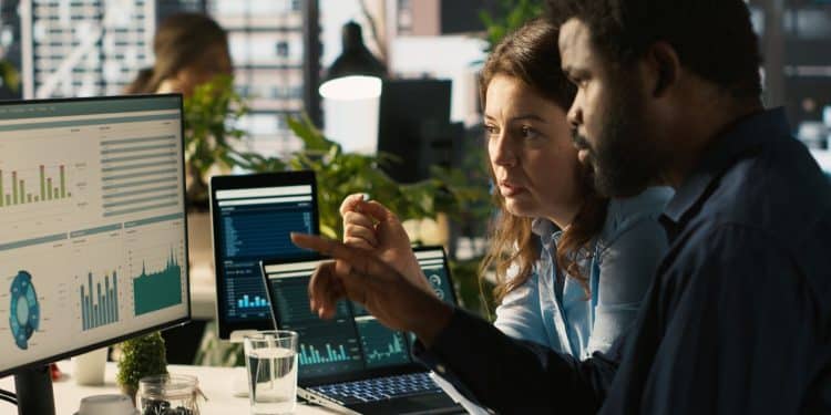 Líder de equipe orientando colaborador sobre ajustes em documentos e gráficos, refletindo o papel de liderar decisões estratégicas baseadas em dados.