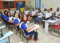 Turma de adultos em sala de aula, com professora ao fundo, representando oportunidades de concurso público para pedagogos.