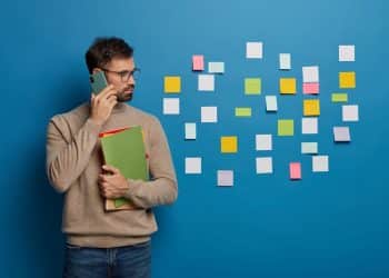 Profissional organizado fala ao celular diante de painel de post-its.