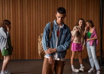 Jovem de jaqueta longe de outras pessoas, com expressão de tristeza.