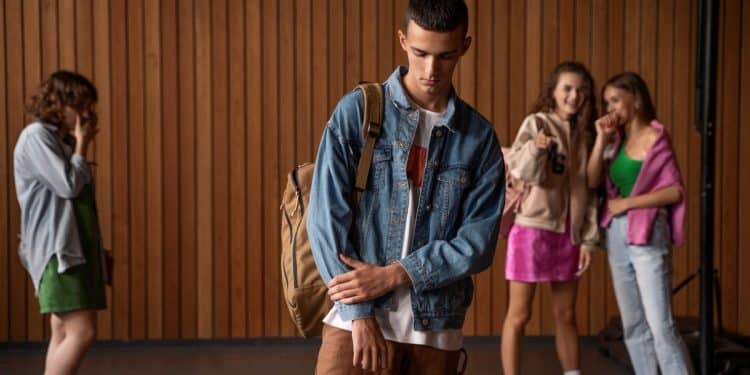 Jovem de jaqueta longe de outras pessoas, com expressão de tristeza.