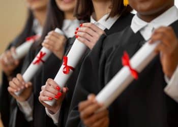 Formandos seguram diplomas com fitas vermelhas em cerimônia.