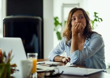 Mulher pensativa, refletindo sobre suas escolhas enquanto calcula seu orçamento, representando a luta interna com o arrependimento e o pensamento sobre o passado.