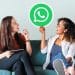 Amigas em sofá seguram placa com logo do WhatsApp sorrindo.