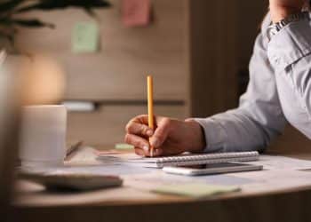 Pessoa escrevendo em caderno enquanto reflete sobre dúvida de português relacionada ao gênero da palavra omelete.