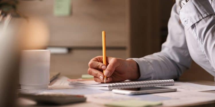 Pessoa escrevendo em caderno enquanto reflete sobre dúvida de português relacionada ao gênero da palavra omelete.
