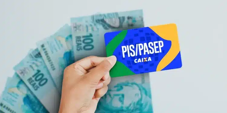 Cartão do PIS/Pasep em mãos, com notas de R$100 ao fundo, representando o pagamento do Abono Salarial de 2026.