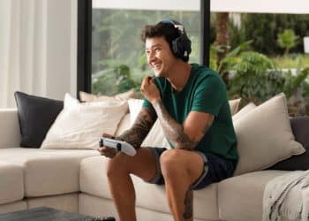 Homem adulto jogando videogame no sofá com fones de ouvido, concentrado e se divertindo em casa.