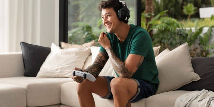 Homem adulto jogando videogame no sofá com fones de ouvido, concentrado e se divertindo em casa.