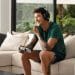 Homem adulto jogando videogame no sofá com fones de ouvido, concentrado e se divertindo em casa.