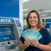 Mulher sorrindo em agência da Caixa segurando dinheiro após saque de benefício com pagamentos para CPFs de 0 a 9.