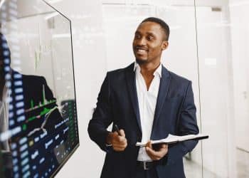 Profissional sorridente fala ao celular enquanto consulta tablet e notebook em escritório moderno