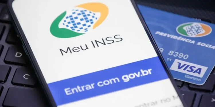 Celular com a tela do aplicativo Meu INSS aberta ao lado de cartão da Previdência Social sobre teclado de notebook