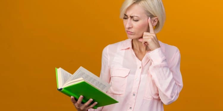 Mulher com expressão pensativa segurando livro verde aberto enquanto reflete antes de retomar os estudos
