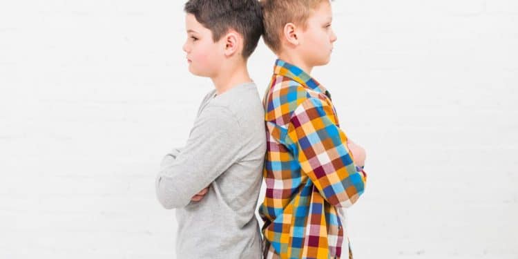 Dois irmãos crianças em posição de costas demonstrando rivalidade infantil causada por comparações familiares.