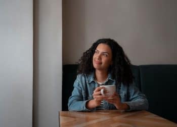 Mulher pensativa segurando uma xícara de café em momento de introspecção e análise mental.