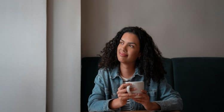 Mulher pensativa segurando uma xícara de café em momento de introspecção e análise mental.