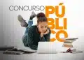 Jovem mulher deitada no chão estudando em notebook ao lado de pilhas de livros e cadernos espalhados