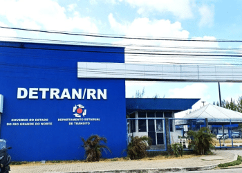 Fachada azul do DETRAN/RN com letreiro branco, brasão do Governo do Estado e uma moto estacionada