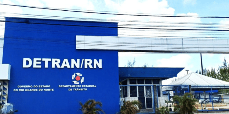 Fachada azul do DETRAN/RN com letreiro branco, brasão do Governo do Estado e uma moto estacionada